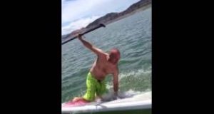 A-man-falls-off-of-a-paddle-board-into-a-lake.